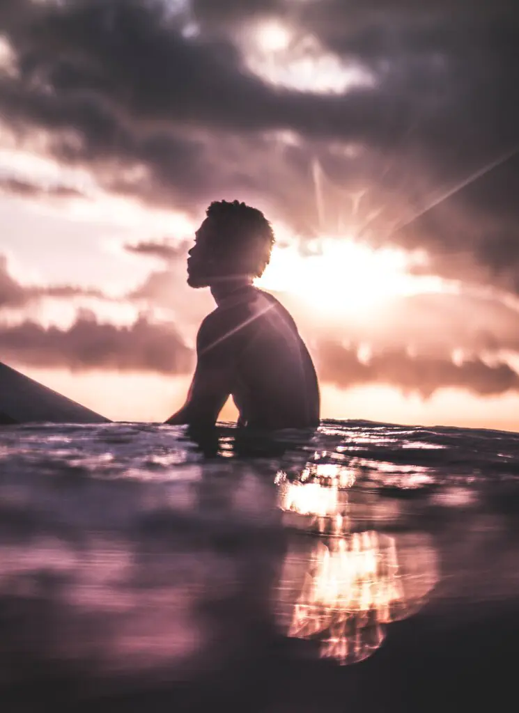 man floating in the water on his surfboard at sunset