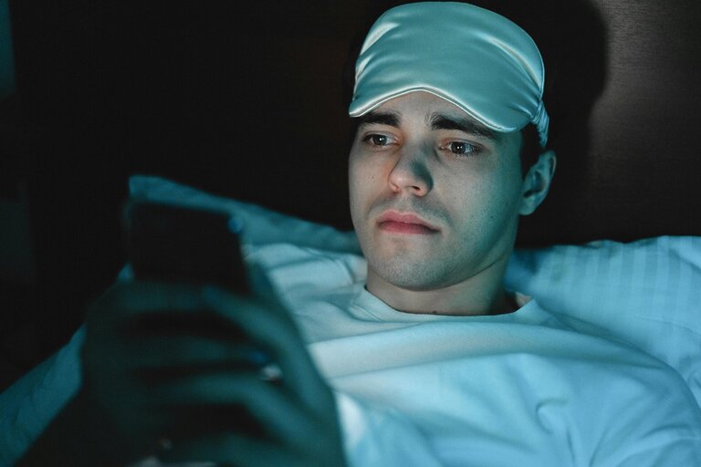 man with sleep mask on his head using his phone, at nighttime