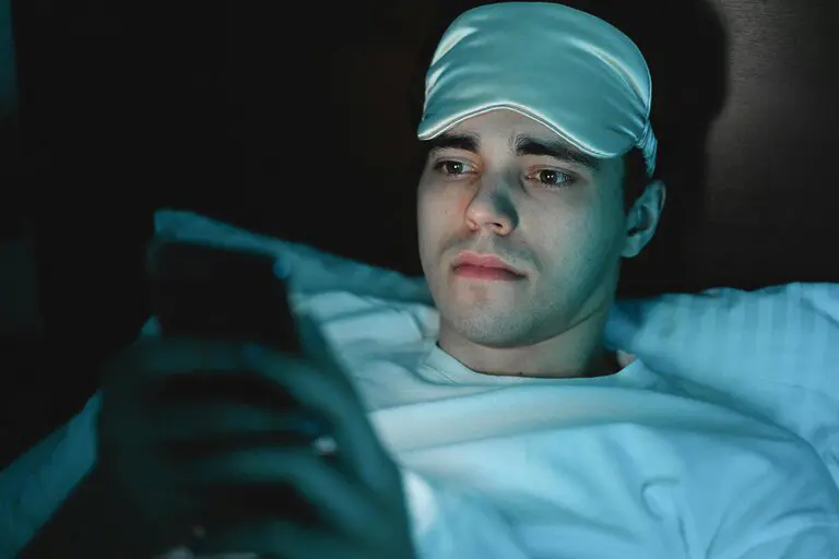 man with sleep mask on his head using his phone, at nighttime